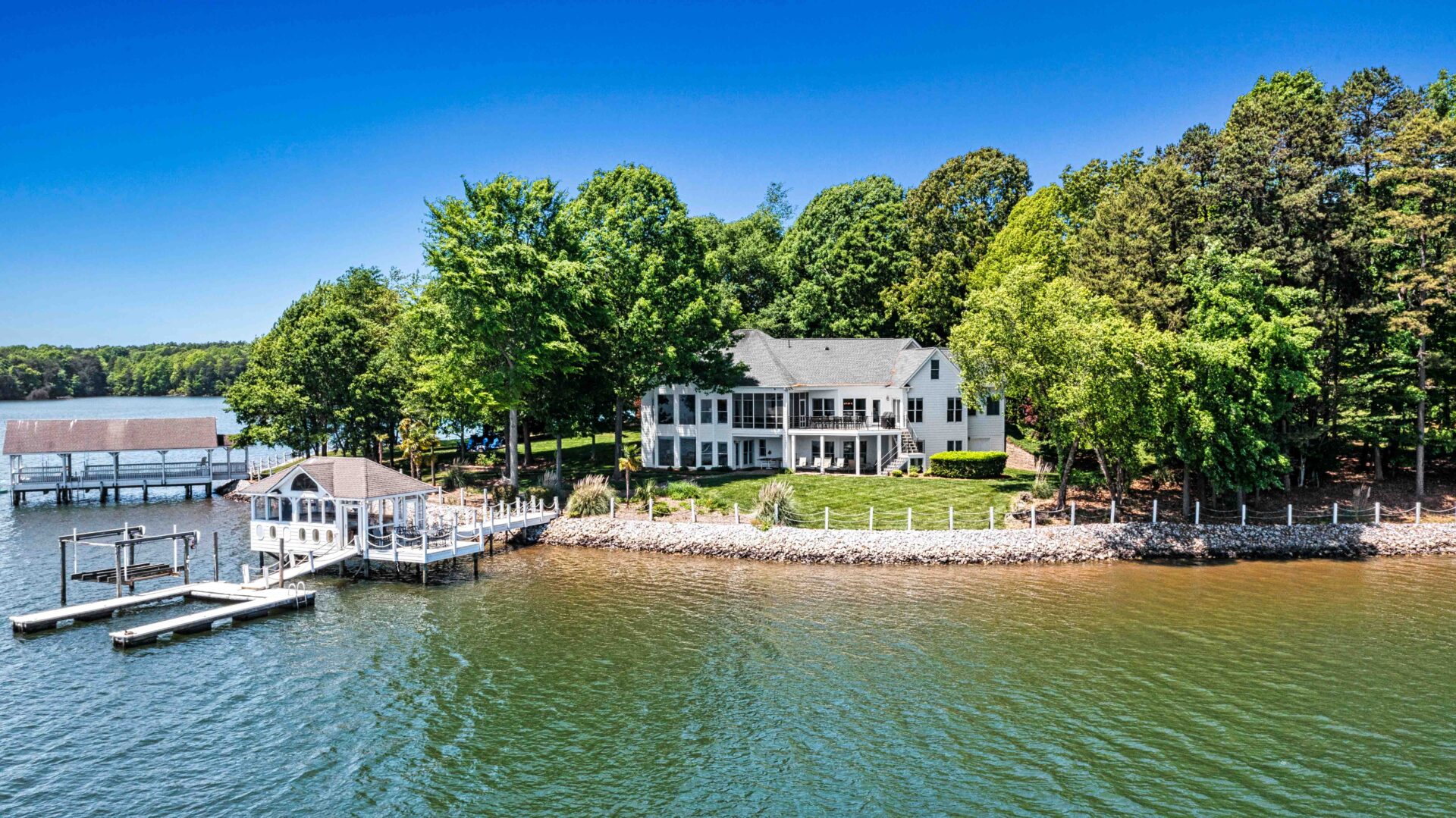 A large house on the water with trees in front of it.